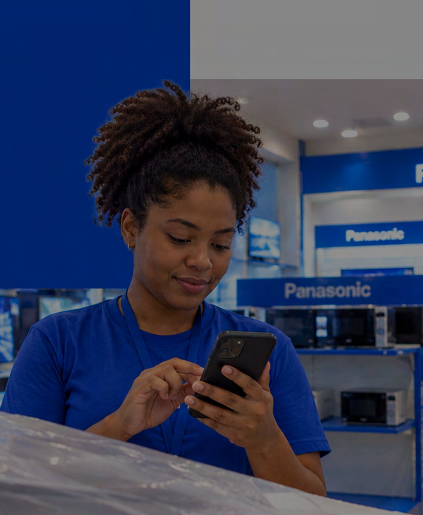 Vendedora com camiseta azul consultando o celular numa loja Panasonic